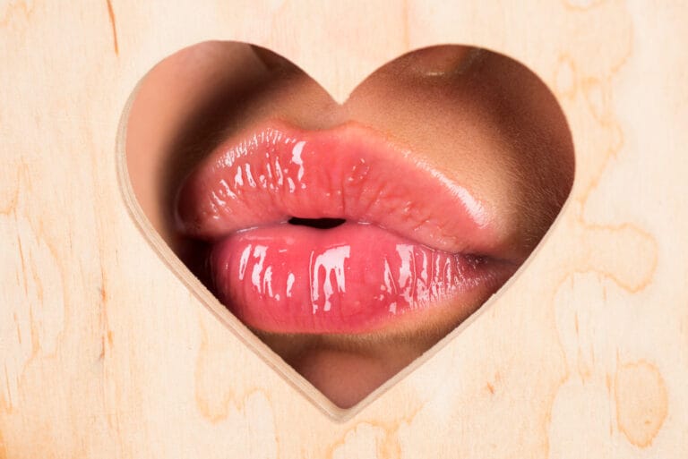 Close-up of glossy lips visible through a heart-shaped cutout in dark wood.