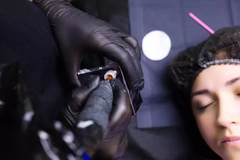 A close-up of a person receiving eyebrow microblading from a technician at Dark Heart Ink, wearing black gloves.