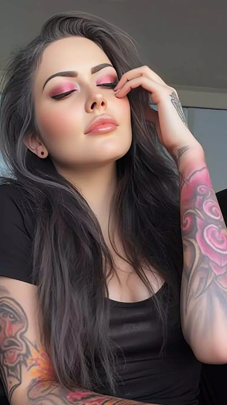 A woman with dark hair and pink eyeshadow poses, showcasing a colorful Winged Eyeliner Tattoo on her arm.