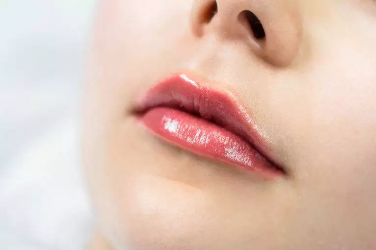 Close-up of a person's lips with a glossy, red lip color, showcasing the benefits of lip blushing.