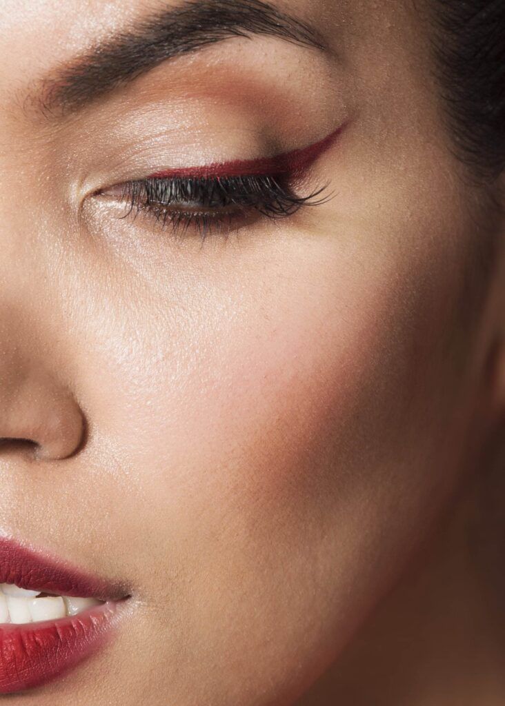 Close-up of a person's face focused on their eye with bold red eyeliner from Dark Heart Ink, smooth skin, and red lipstick.