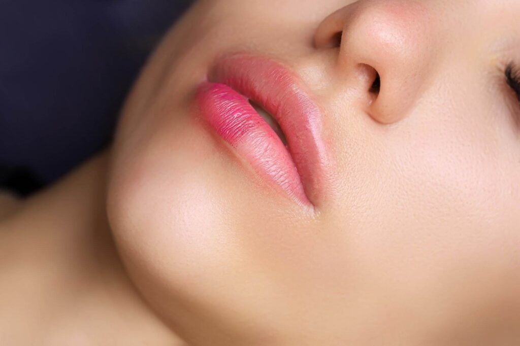 Close-up view of a person's lips and nose, highlighting the smooth skin, natural makeup, and perfect pout achieved through lip blushing.