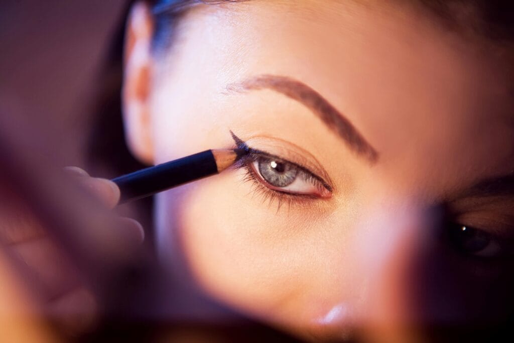 Close-up of a person applying black eyeliner pencil to their upper eyelid, focusing on the eye and eyebrow—discover the benefits of Permanent Eyeliner in East Bay for long-lasting, flawless definition.
